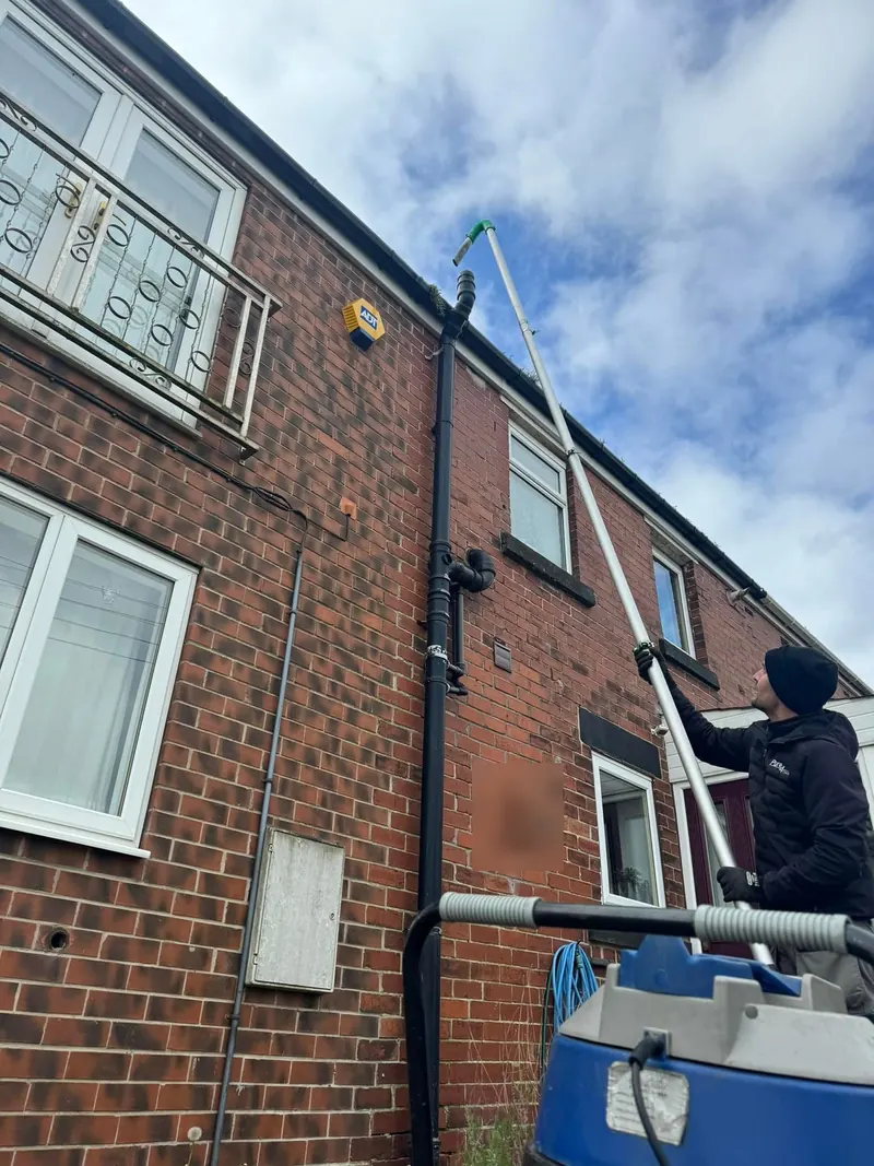 Gutter vacuum pole clearing the gutter of a red brick house